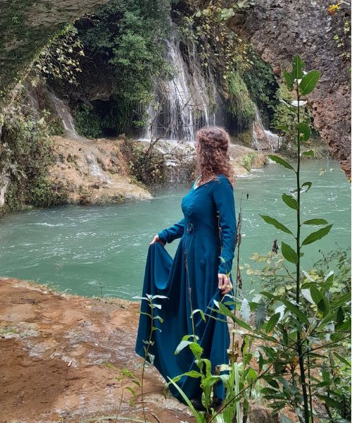Une femme en robe médiévale bleue debout sous un pont de pierre près d'une rivière