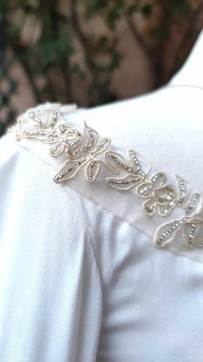 Détails du ruban brodé doré et perles argent à l'encolure d'une robe fantasy blanche sur mannequin