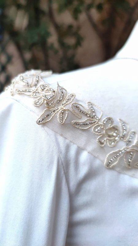 Détails du ruban brodé doré et perles argent à l'encolure d'une robe fantasy blanche sur mannequin