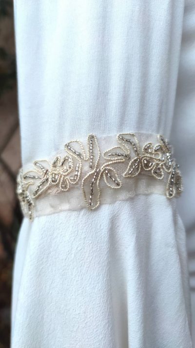 Détails du ruban brodé doré et perles argent au bras d'une robe fantasy blanche sur mannequin