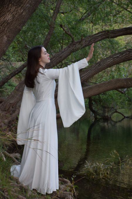 Femme en robe blanche medievale faisant signe d'arrêter avec sont bras tendu paume ouverte