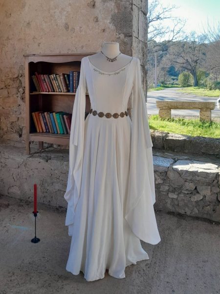Robe medieval fantasy blanche de princesse sur un mannequin devant un porche ancien