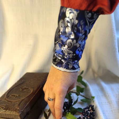 Manchette en brocard bleu et argent aux motifs fleur de lys, portée au poignet sur la manche