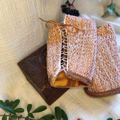 Fermeture à lacets de manchons de poignets en tissu brocard de style fantasy de conte de fée posée sur un tissu crème à côté de branchages portant des baies rouges et noires