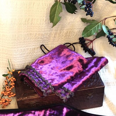 manchons de poignet fantasy de conte de fée en velours pourpre décorée d'un galon brodé or, posée sur un tissu crème à côté de petites branches avec des bais colorées