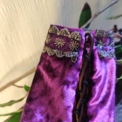 fermeture à lacets de en gros plan de manchons de poignets fantasy de conte de fée en velours pourpre décorée d'un galon brodé or, posée sur un tissu crème à côté de petites branches avec des bais colorée