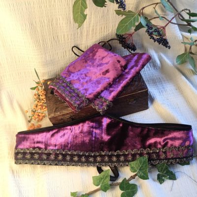 Ensemble brassards et Ceinture fantasy de conte de fée en velours pourpre décorée d'un galon brodé or, posée sur un tissu crème à côté de petites branches avec des bais colorées