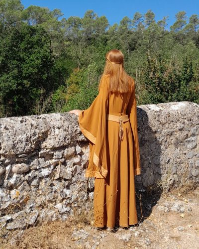 Femme portant une robe Isolde médiévale fantasy couleur cannelle vue de dos sur un pont ancien
