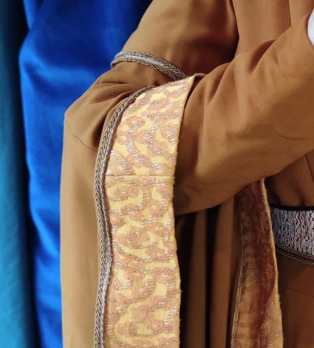 Gros plan sur le brocard qui borde la surmanche de Robe médiévale couleur carmel portée