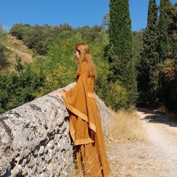Femme rousse portant une robe médiévale fantaisie couleur cannelle vue de côté sur un pont en Pierre