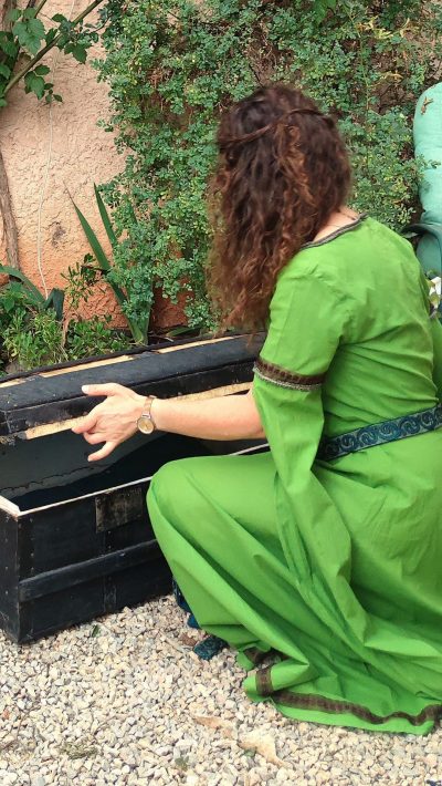 Robe médiévale fantasy vert anis portée par une femme accroupie de dos qui ouvre un coffre en bois