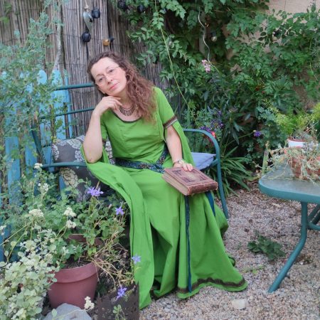 Robe médiévale fantasy vert anis portée par une femme assise pensive un livre à la main dans un jardin
