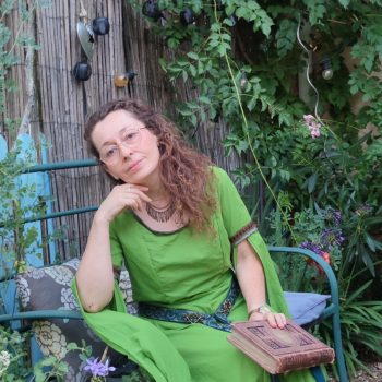 Robe médiévale fantasy vert anis portée par une femme assise pensive un livre à la main dans un jardin