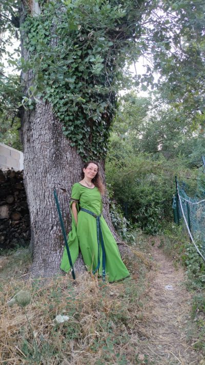 Robe médiévale fantasy vert anis portée par une femme debout adossée à un chêne pluricentenaire