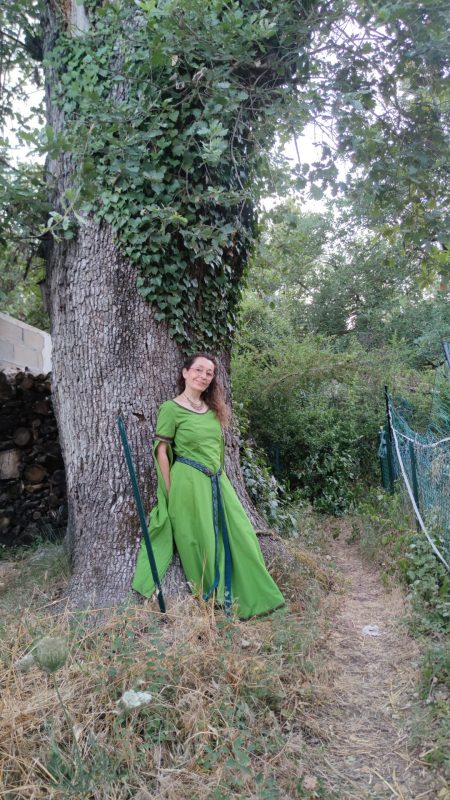Robe médiévale fantasy vert anis portée par une femme debout adossée à un chêne pluricentenaire