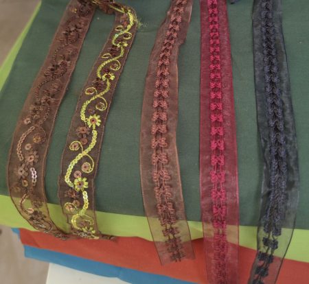 échantillons de différents galons brodés posés sur une pile de 4 tissus de couleurs différentes pour le choix des galons de la robe médiévale fantasy Eirien