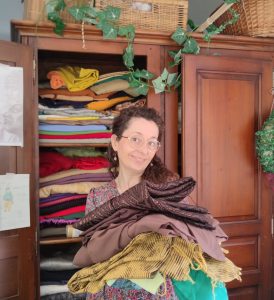 Couturière portant une pile de tissu devant son armoire remplie de textiles