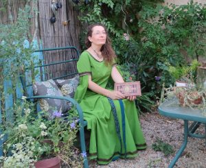 Femme avec une robe médiévale verte assise dans un jardin et tenant un livre